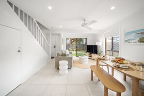 Ein modernes Interieur mit einer Treppe, einer Essecke mit Tisch und Bank, einem Sofa und einem Fernseher.