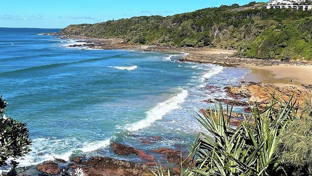A coastal landscape with a beach, rocky shoreline, and vegetation.