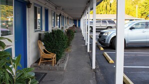 A motel with a covered walkway, parked cars, and a chair outside. - Stevenson Motel Federal Way Near I 5 (Federal Way)