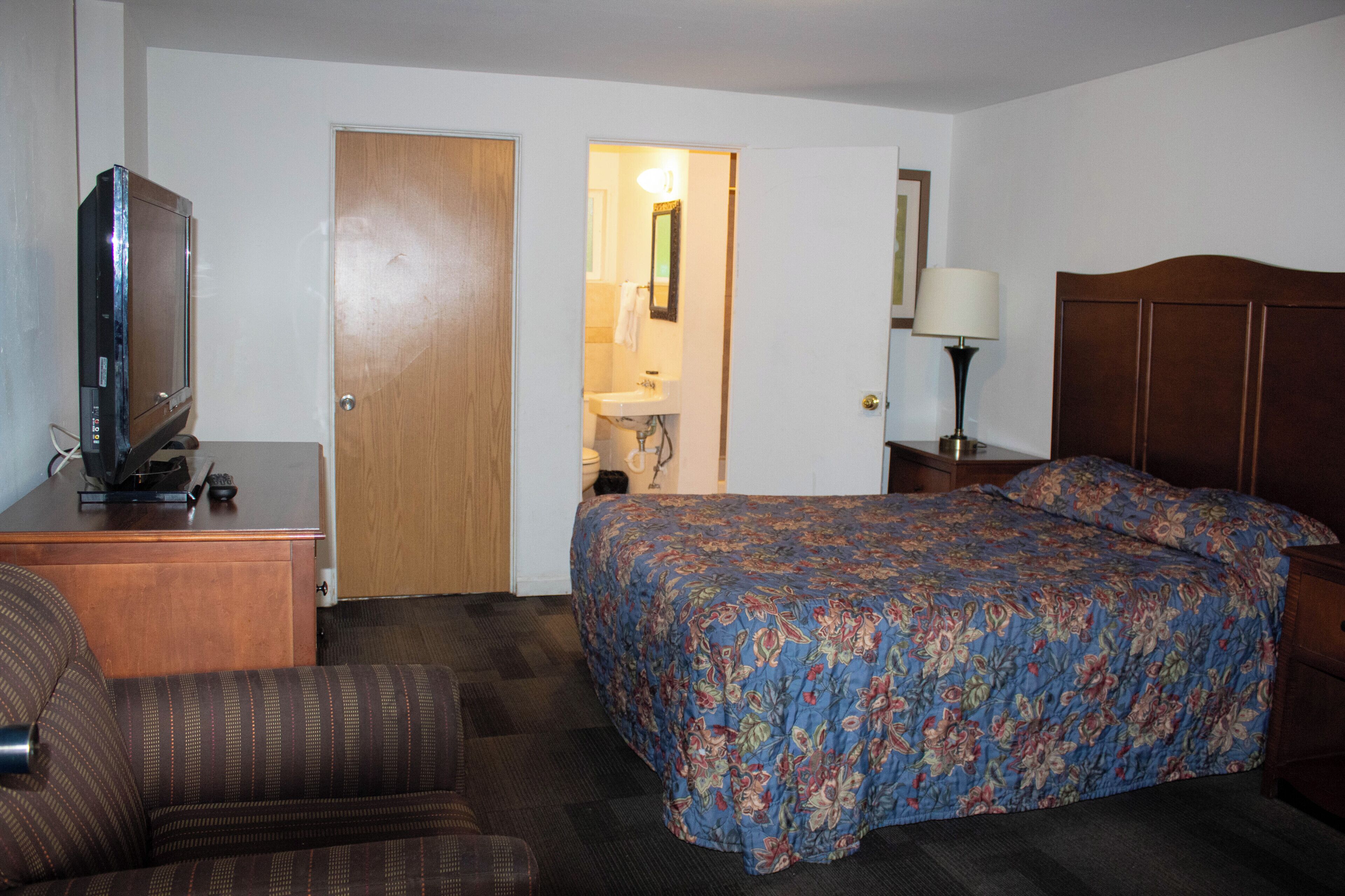 Habitación de hotel con una cama, un televisor sobre un escritorio, una silla y un baño visible a través de una puerta abierta.
