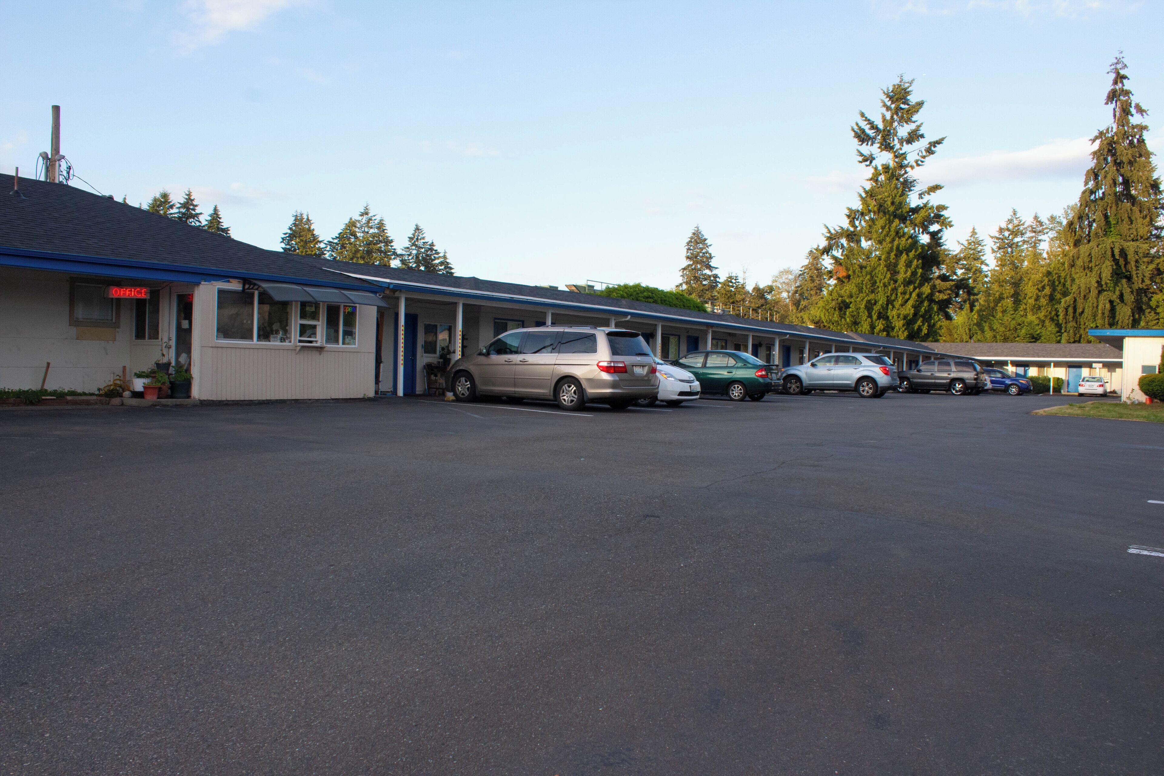Un motel con estacionamiento, varios autos estacionados y una fila de habitaciones con techo azul.