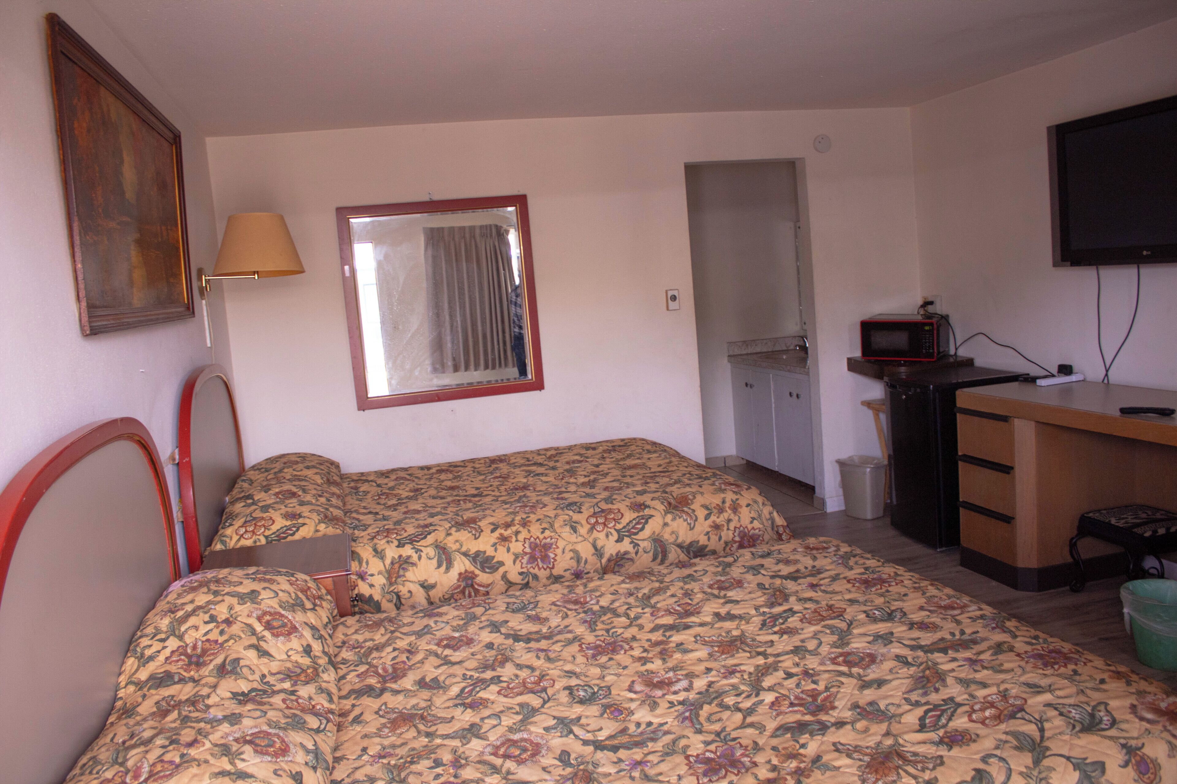 A bedroom with a bed, a desk, a television, and a mirror.