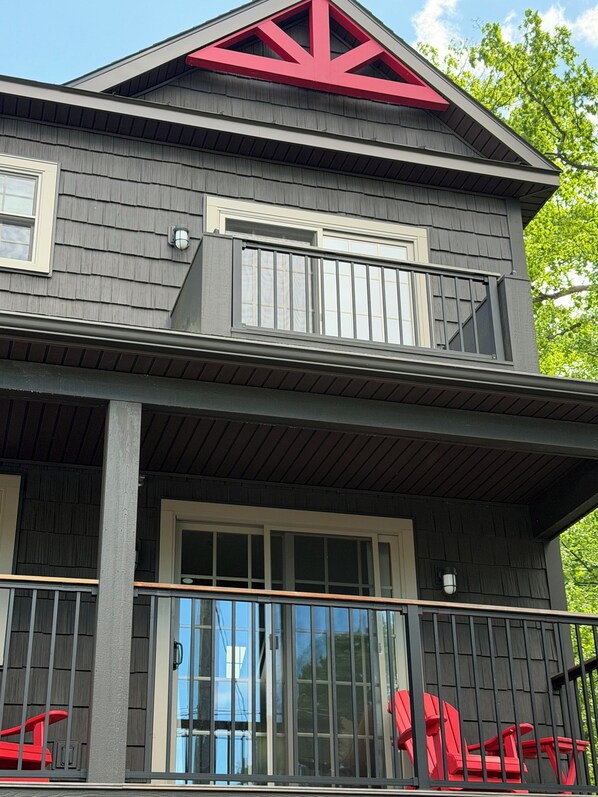 Una casa de dos pisos con balcón, ventanas grandes y un diseño de techo rojo en forma triangular.