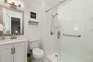 Un baño con lavamanos blanco, inodoro, ducha con mampara de vidrio y espejo con luz.