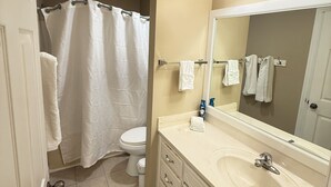 Un baño con inodoro, cortina de ducha, lavabo, espejo y toallero.