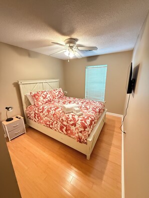 A bedroom with a bed, a nightstand, a ceiling fan, a window with blinds, and a wall-mounted TV. - Cozy Townhome in Marietta! (Marietta)