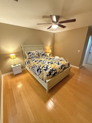 Une chambre à coucher comprenant un lit, deux tables de chevet, un ventilateur de plafond et une petite table d’appoint.