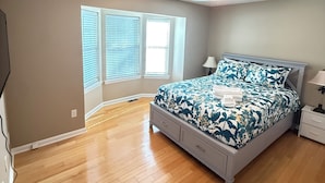 Un dormitorio con cama, ventilador de techo, ventana con persianas y mesita de noche.