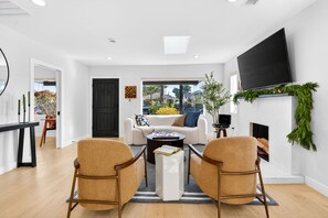 Un salon moderne comprenant un canapé, deux fauteuils, une table basse, un téléviseur à écran plat, une cheminée et une vue sur l’extérieur grâce à une porte vitrée.