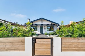 Une maison moderne avec un portail en bois, un porche et un ciel dégagé.