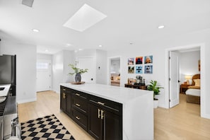 A modern kitchen with a central island, a dining area, and a bedroom with a bed and bedside table.