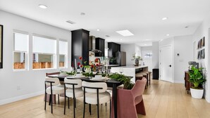 A modern kitchen with dark cabinets, a dining area with white chairs, and a large window. - Unique Downtown LA Gem: World Cup, SoFi, Gym & Games - 2 suites (Los Angeles)