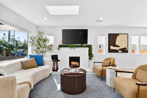 A modern living room with a sofa, armchairs, a coffee table, a fireplace, a TV, and artwork on the walls.