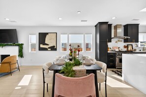 A modern kitchen with dark cabinets, a central island, and a dining area with a table set for six. - Unique Downtown LA Gem: World Cup, SoFi, Gym & Games - 2 suites (Los Angeles)