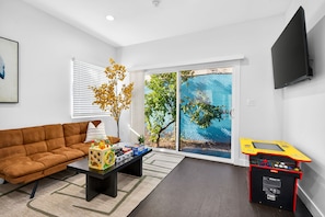 A living room with a brown sofa, a coffee table with toys, a TV, and a sliding glass door to a garden.