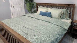 Une chambre à coucher avec un lit en bois, une porte blanche, une grande plante et un tableau accroché au mur.