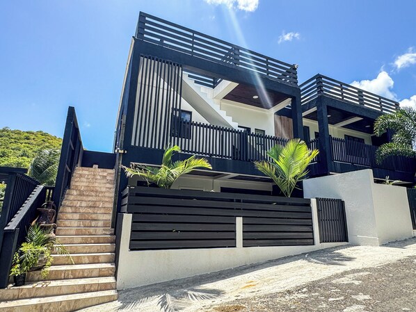 A modern two-story house with a staircase, a balcony, and a view of the sky.