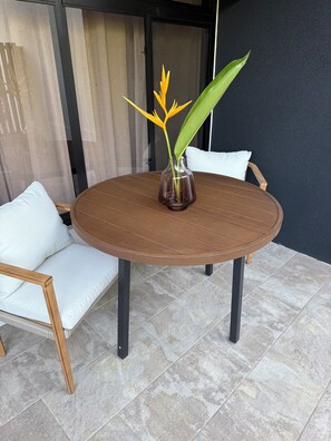 Una mesa redonda de madera con un florero de vidrio que contiene una planta, rodeada de sillas blancas con cojines.