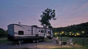 A recreational vehicle parked in a grassy area with outdoor seating and string lights.
