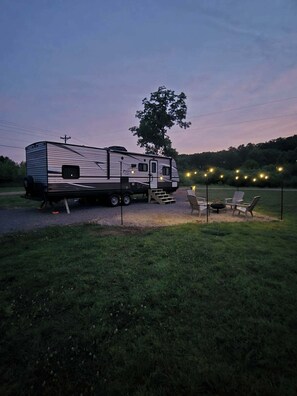 Una autocaravana estacionada en un césped con mobiliario exterior e iluminación colgante.