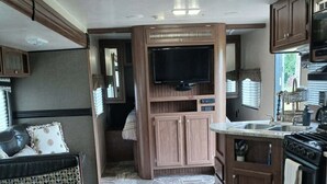 A compact RV kitchen with a built-in stove, a television, and a dining area with a bench.