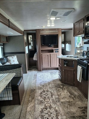 Cocina compacta para autocaravana con estufa integrada, televisor y zona de comedor con banco.