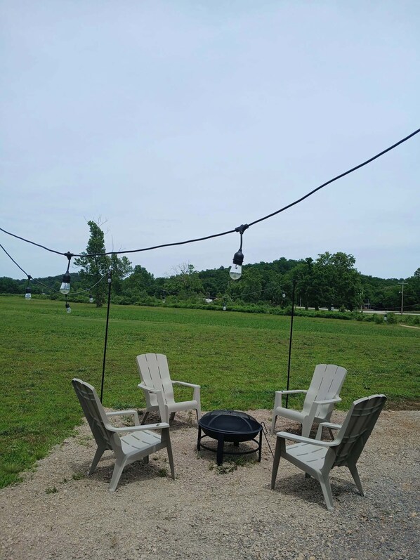 Two outdoor seating areas with chairs and a table, surrounded by a grassy field and trees, under a string of lights. - Creekside Family camping near Clearwater Lake! (Piedmont)
