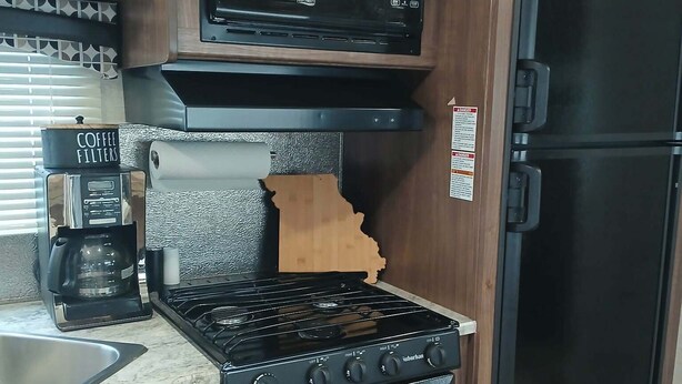 A kitchen with a black microwave, stove, and refrigerator, with a coffee maker and a sink.