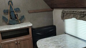 A compact kitchen with a marble countertop, wooden cabinets, a black leather bench, and a hanging anchor decoration.