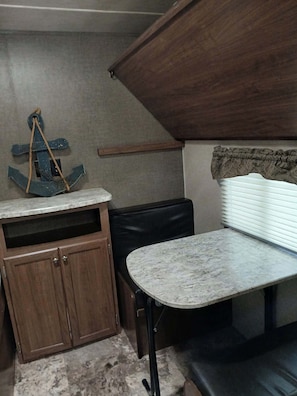 Cocina compacta con encimera de mármol, armarios de madera, un banco de cuero negro y un adorno con forma de ancla colgante.