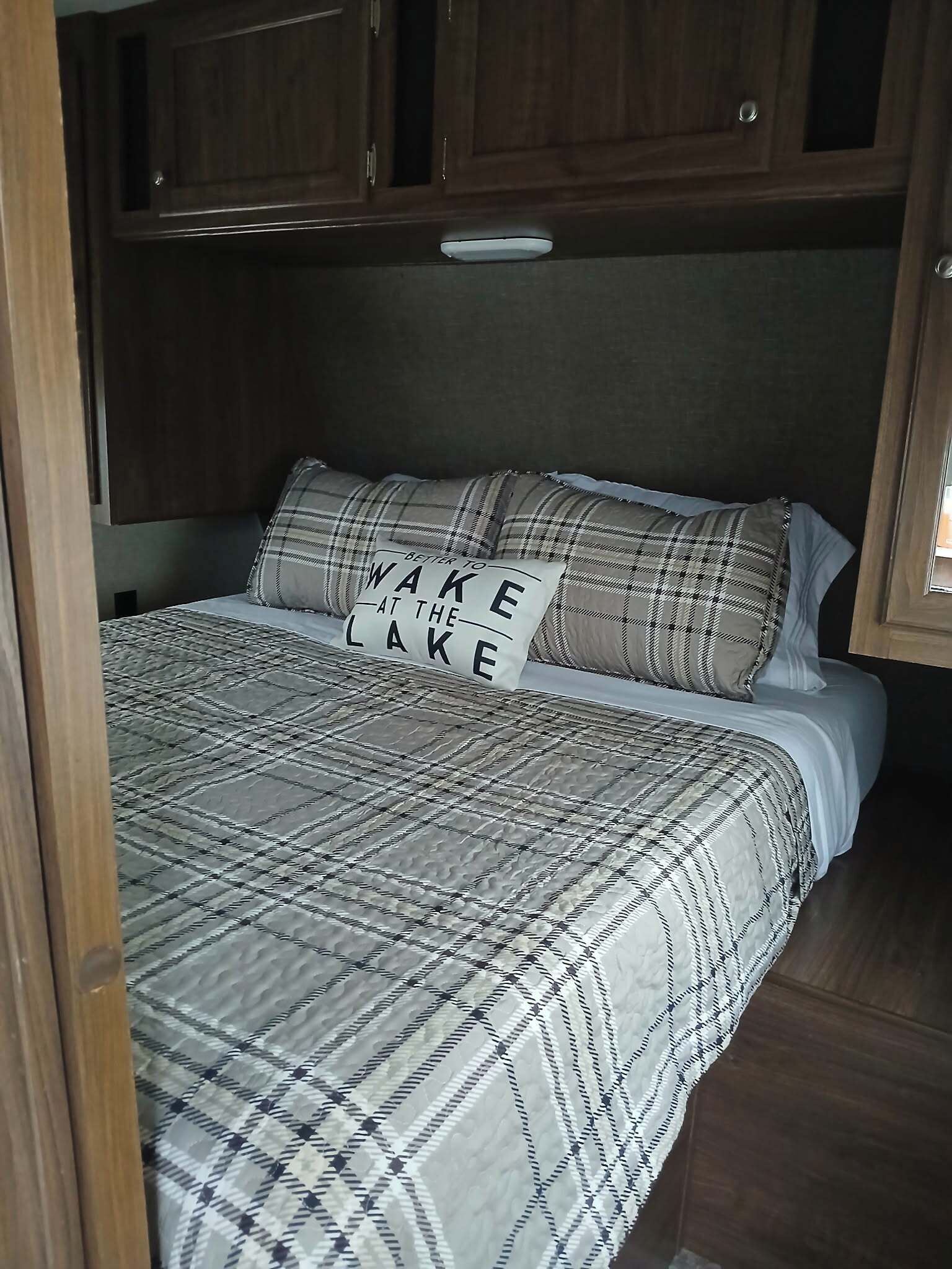 A bed with a plaid bedspread and pillows, a headboard, and wooden cabinets above.