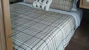 A bed with a plaid bedspread and pillows, a headboard, and wooden cabinets above.