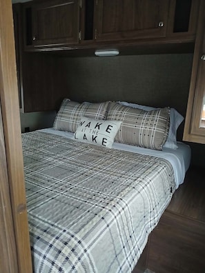 Una cama con colcha y almohadas de cuadros, un cabecero y armarios de madera encima.