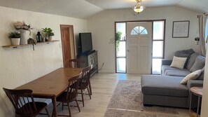 A cozy living room with a dining area, a grey sofa, and a television on a wooden cabinet. - Family-Friendly 3bdr Coastal Retreat Near Beaches & Redwoods (Watsonville)