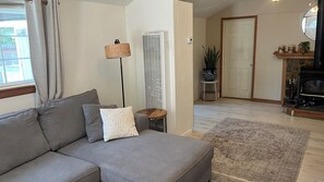 Ein Wohnzimmer mit grauem Sofa, einer Stehlampe, einem kleinen Tisch, einer Topfpflanze und einem Kamin.