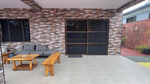 Un espace patio agrémenté d’un mur en briques, d’une porte-fenêtre coulissante, d’un canapé gris et de meubles en bois.
