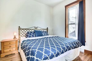 Une chambre à coucher avec un lit, une table de chevet, une fenêtre et une vue sur une maison.