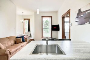 A modern kitchen with a central island, a sofa, a dining table, and a TV mounted on the wall.