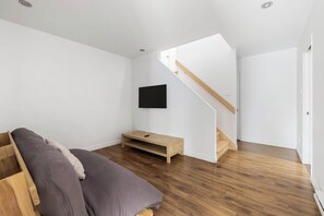 A bedroom with a bed, a TV mounted on the wall, a wooden bench, and a staircase.