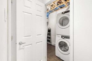 A laundry room with two stacked front-loading washing machines, a metal drying rack, and a white door.