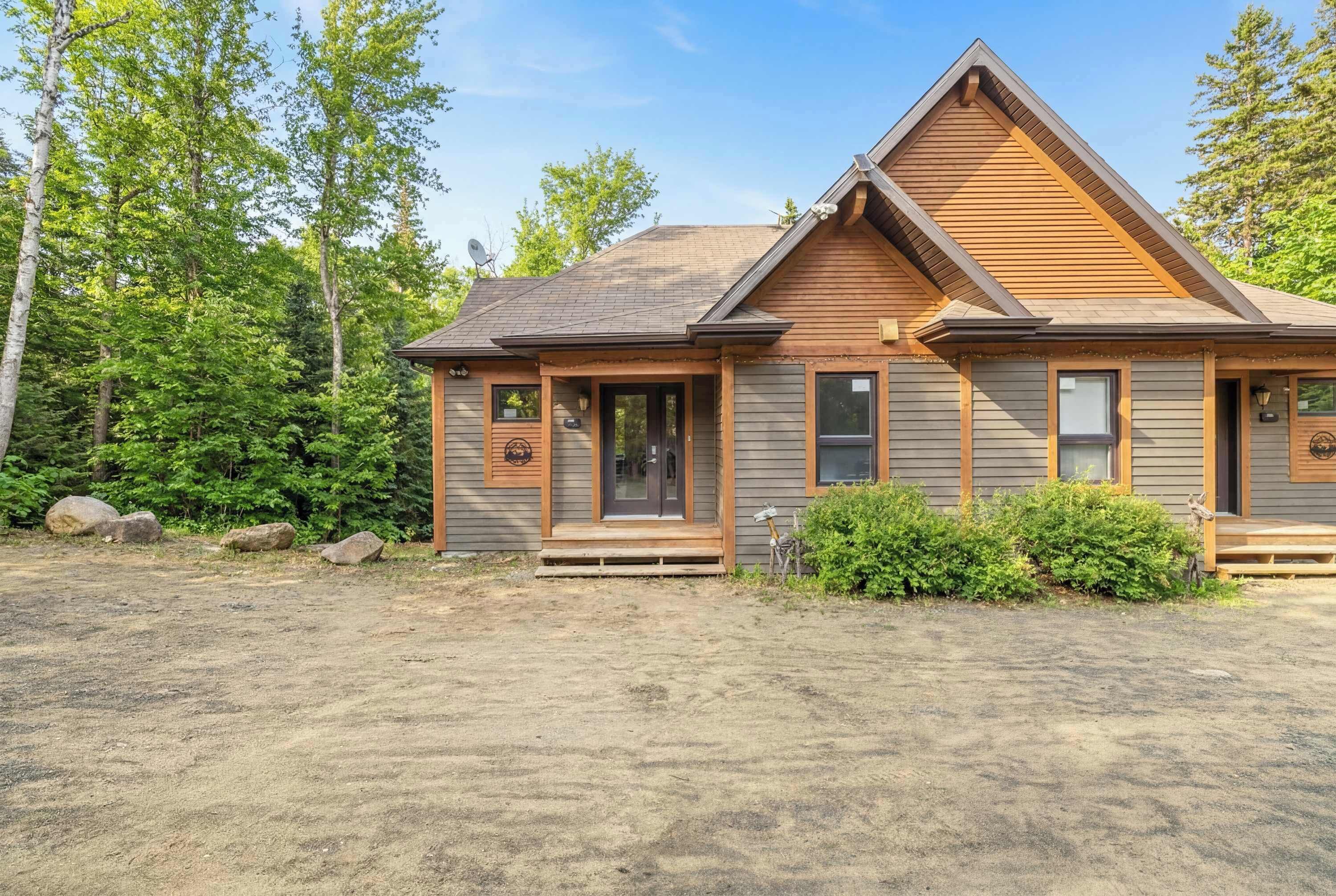 A two-story cabin with a front porch, a garage, and a large window.