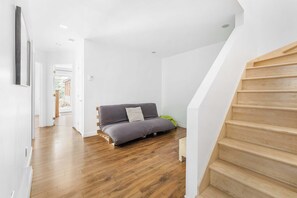 A modern interior with a wooden staircase, a grey sofa, and a wooden floor.