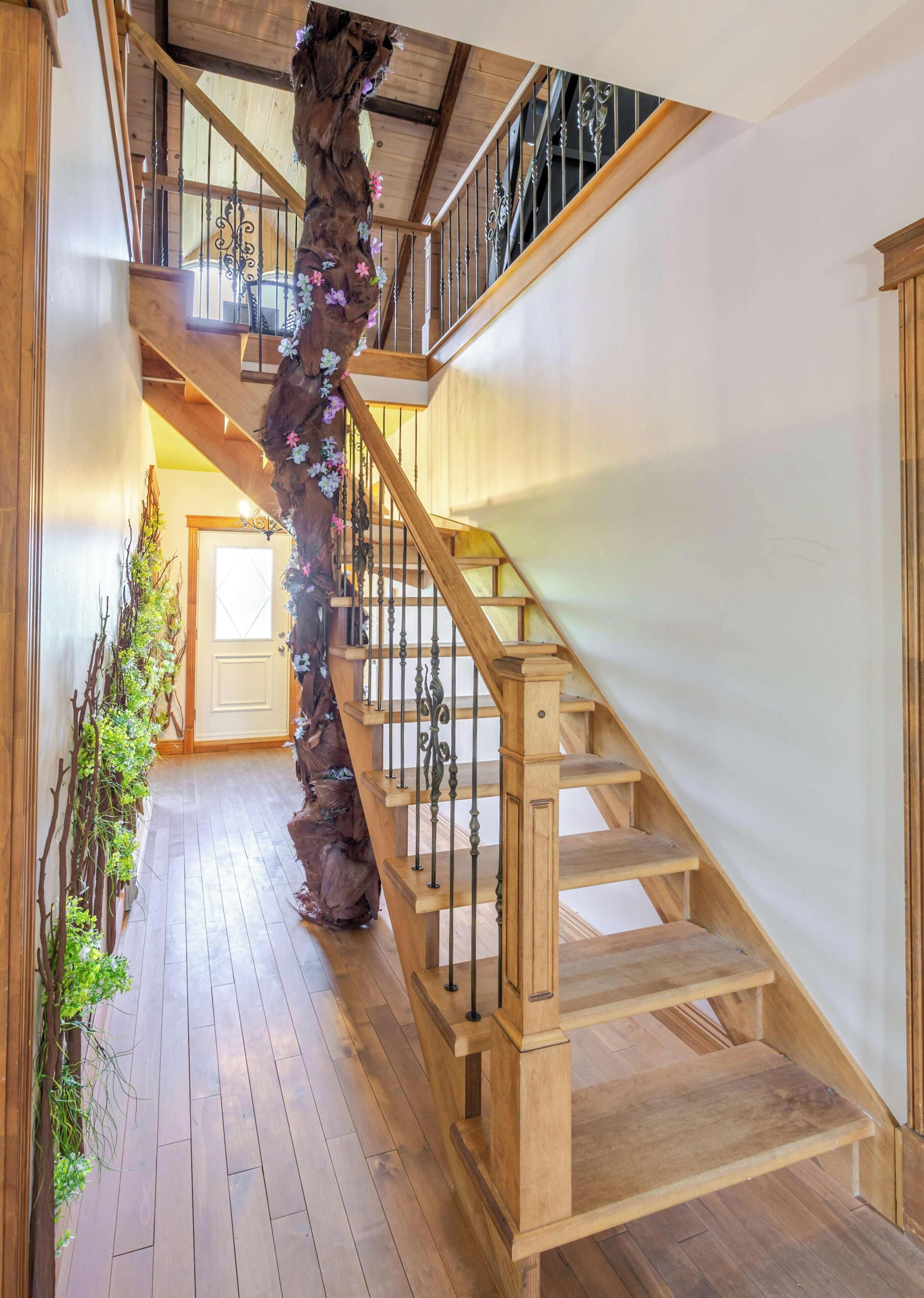 A wooden staircase with a decorative tree trunk and metal balusters.