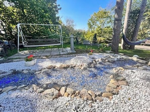 A garden with a swing set, a hammock, and a small water feature with pebbles.