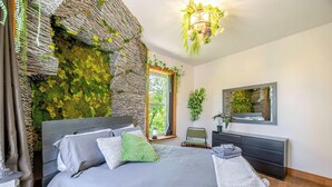 A bedroom with a bed, a bedside table, a mirror, and a window with a view of greenery. - Chateau De Valvak  Spa & BBQ  Free Parking (Lévis)