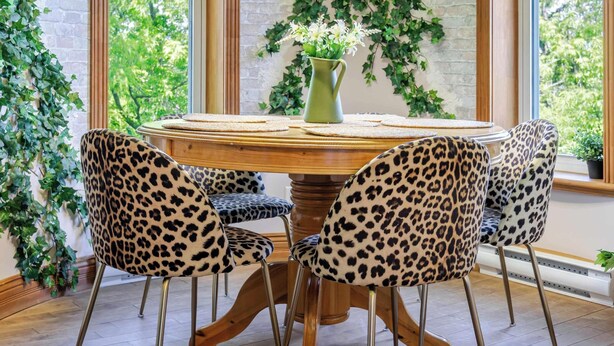 A dining area with a round table, leopard print chairs, a hanging light fixture, and a brick wall with ivy. - Chateau De Valvak  Spa & BBQ  Free Parking (Lévis)