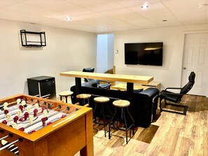 Una habitación con mesa de fútbol, televisor, sofá y zona de bar.