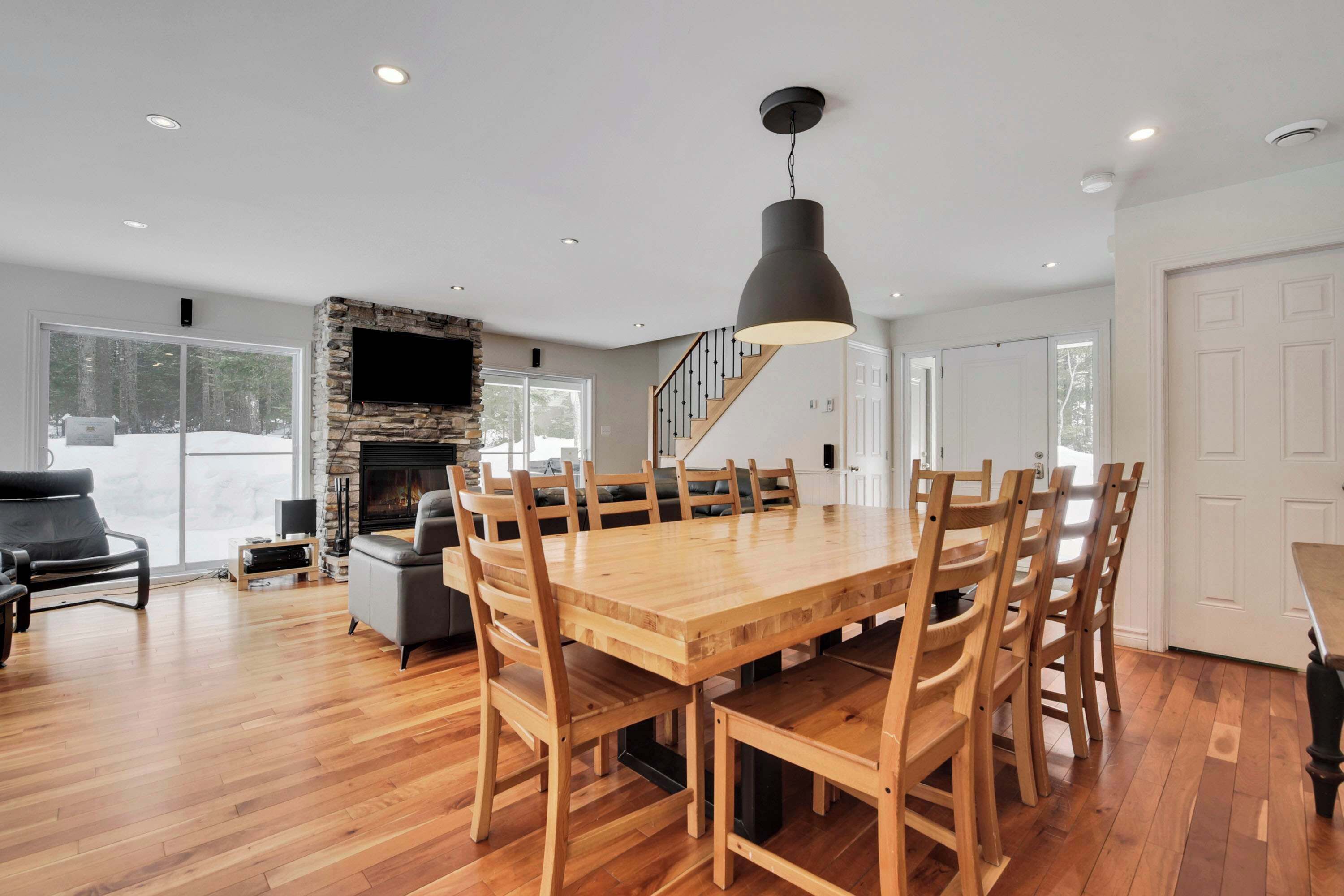 A spacious dining area with a large wooden table and chairs, a stone fireplace, and a modern pendant light.