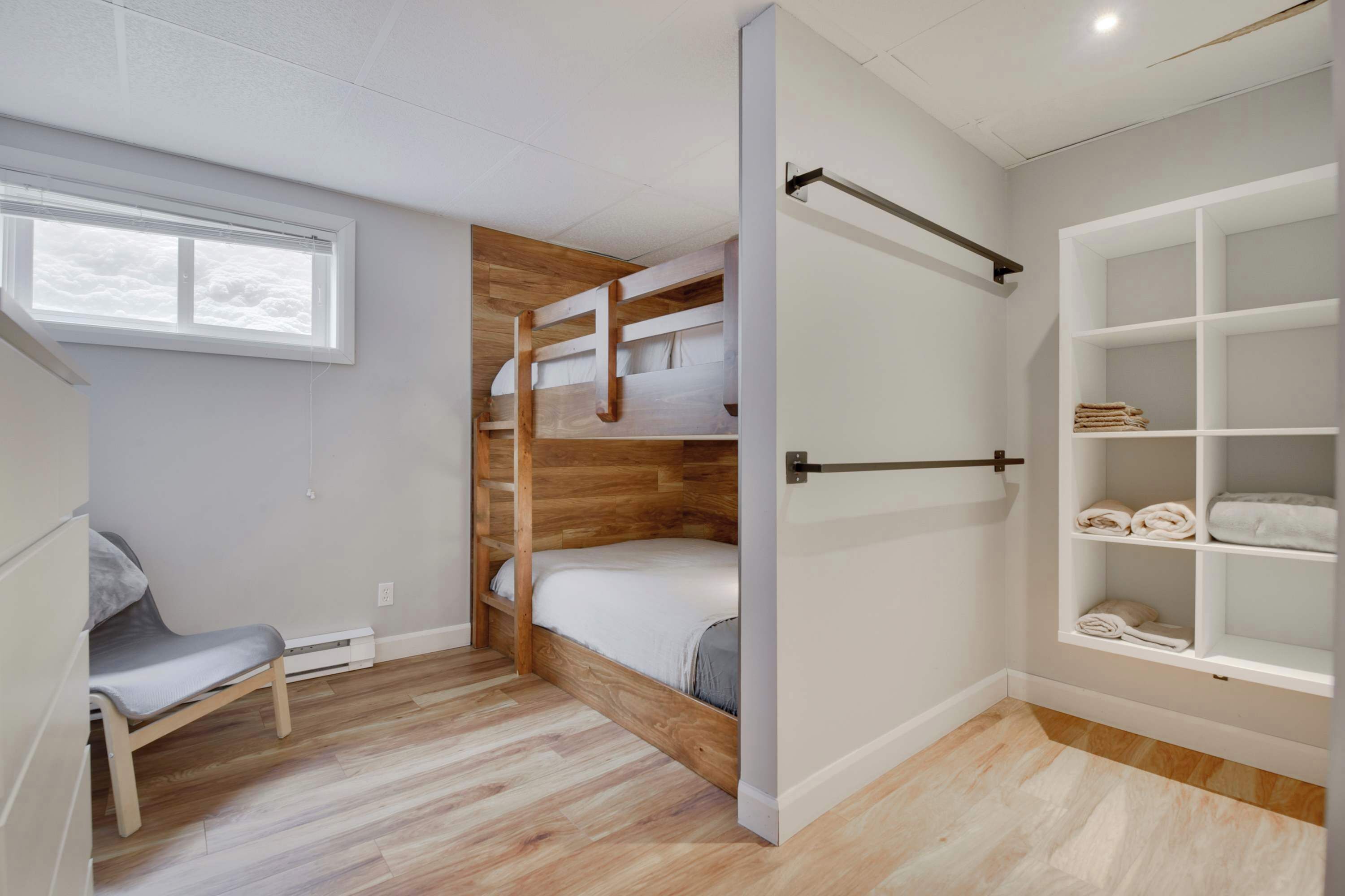A room with a bunk bed, a chair, a white wardrobe, and a window.