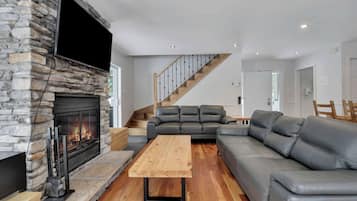 A modern living room with a stone fireplace, leather sofas, a wooden coffee table, and a staircase.